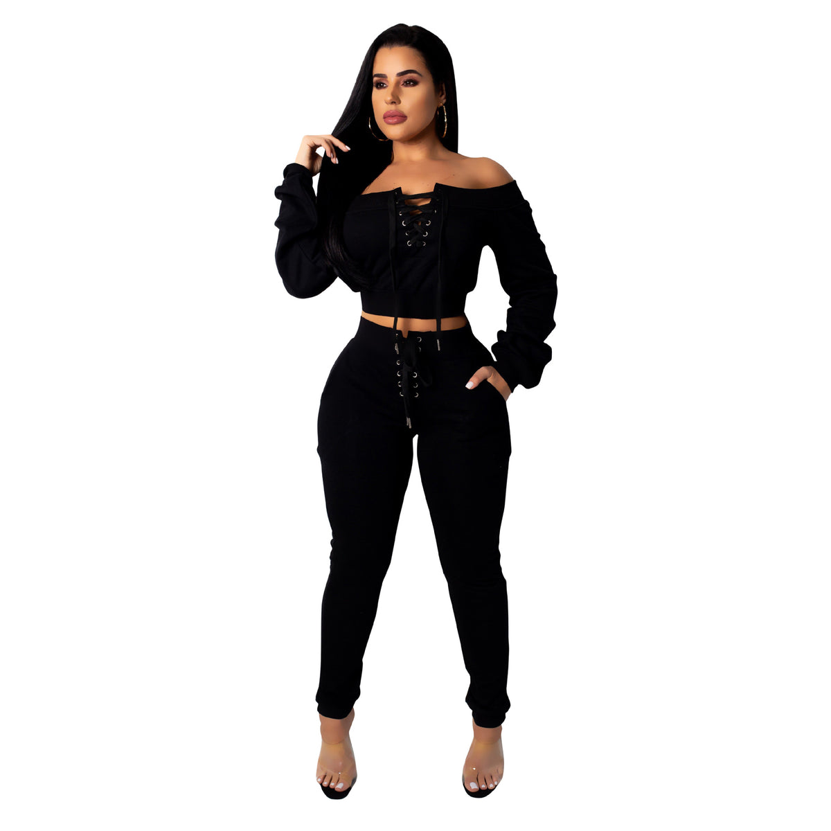 Woman wearing a Black off-shoulder lace-up cropped top with matching Black jogger pants and heels against a white background.