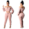 Woman shown in front and back views wearing a Pink off-shoulder lace-up cropped top with matching Pink jogger pants and clear heels against a white background.