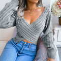 Woman seated indoors wearing a heather gray twist-front V-neck cropped knit sweater with blue jeans.