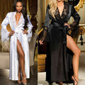 Side-by-side full-length comparison of the Seraphina women's long satin-look robe in white and classic black, modeled by two women in an elegant indoor setting. The white robe features delicate white floral lace trim along the deep V-neckline, a matching waist sash, relaxed long sleeves, and a flowing maxi-length skirt with an open front. The black version showcases glossy dark fabric, intricate black lace detailing, a tied waist belt, and a dramatic floor-length silhouette.