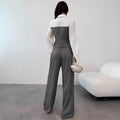 Back view of the Sloane women's gray tailored pants set, featuring a fitted sleeveless vest layered over a white long-sleeve blouse, a shaped waist, and matching high-waisted gray wide-leg trousers extending to the floor.