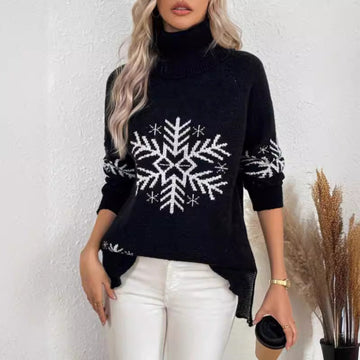 Woman wearing a Black Snowfall Luxe Turtleneck Holiday Sweater with a large white snowflake design, white pants, and a small black handbag.