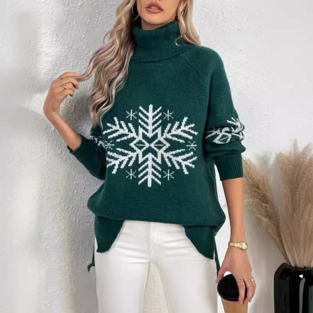 Woman wearing a Black Snowfall Luxe Turtleneck Holiday Sweater with a large white snowflake design, white pants, and a small black handbag.