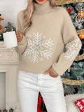 Woman wearing a Khaki Snowfall Luxe Turtleneck Holiday Sweater with a large white snowflake design and white pants beside a decorated Christmas tree.