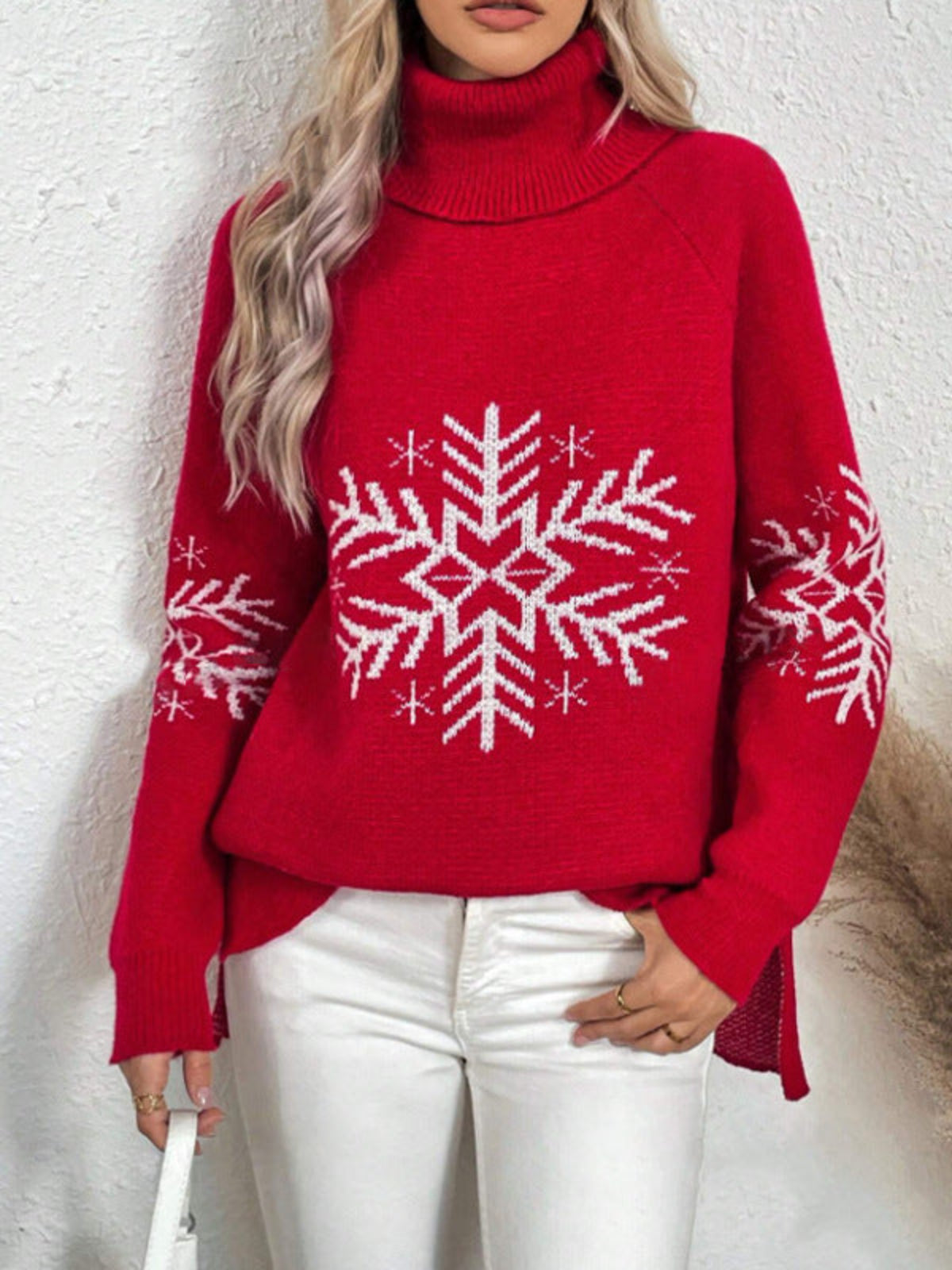Woman wearing a Red Snowfall Luxe Turtleneck Holiday Sweater with a white snowflake design on the front and sleeves, paired with white pants.