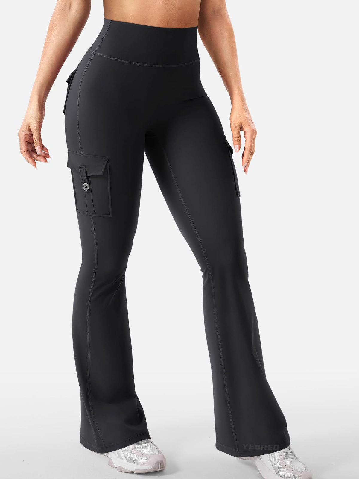Talia women's black high-waisted flare active pants shown on a model, featuring a fitted waistband, smooth body-contouring silhouette through the hips and thighs, decorative back flap pockets with button-style closures, and long fitted pant legs that gradually widen into a fashionable flared hem.