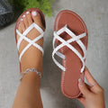 White women’s braided toe-ring flat sandals featuring slim woven crossover straps, an open-toe silhouette, warm brown footbed with contrast stitching, shown with one sandal worn and the matching sandal held beside it for a close-up view of the strap construction.