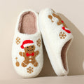 White gingerbread Christmas plush slippers for women shown from a side product angle, highlighting the fuzzy closed-toe construction, embroidered gingerbread and snowflake decorations, soft plush lining, rounded silhouette, and cozy indoor slipper design.