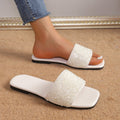 White women’s rhinestone flat slide sandals featuring a shimmering embellished upper, open-toe design, smooth white footbed, and slim flat sole, shown with one sandal worn and the matching sandal positioned beside it to display the sparkling strap and side profile.