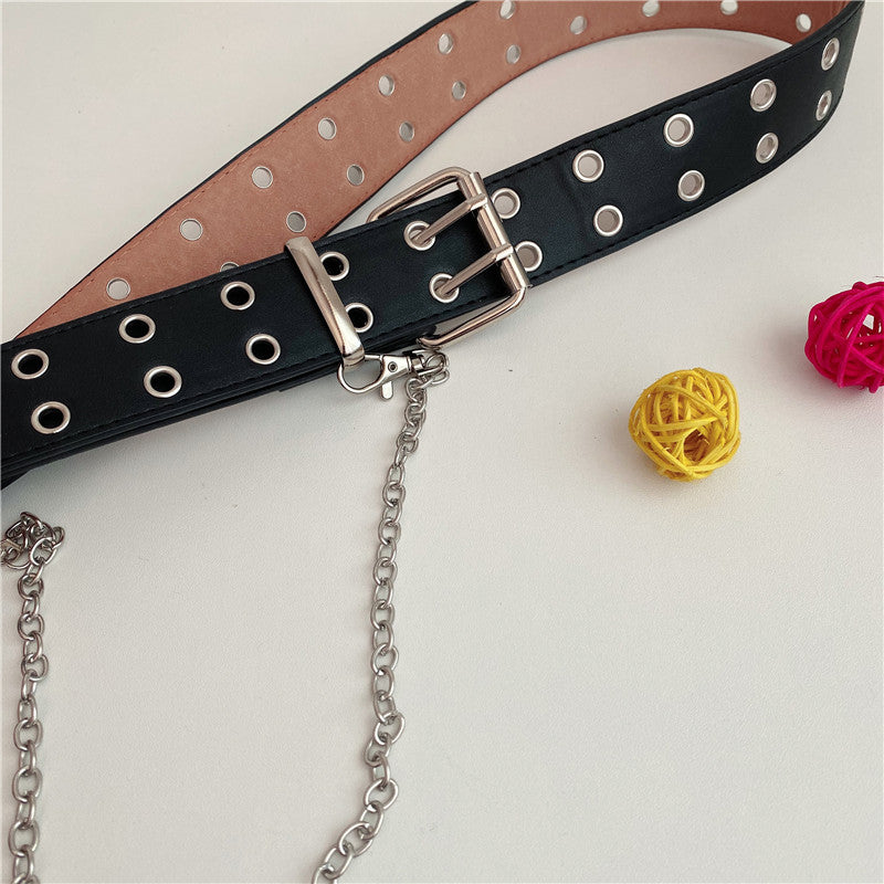 Close-up of women’s black grommet belt with silver-tone buckle, metal eyelets, and chain detail