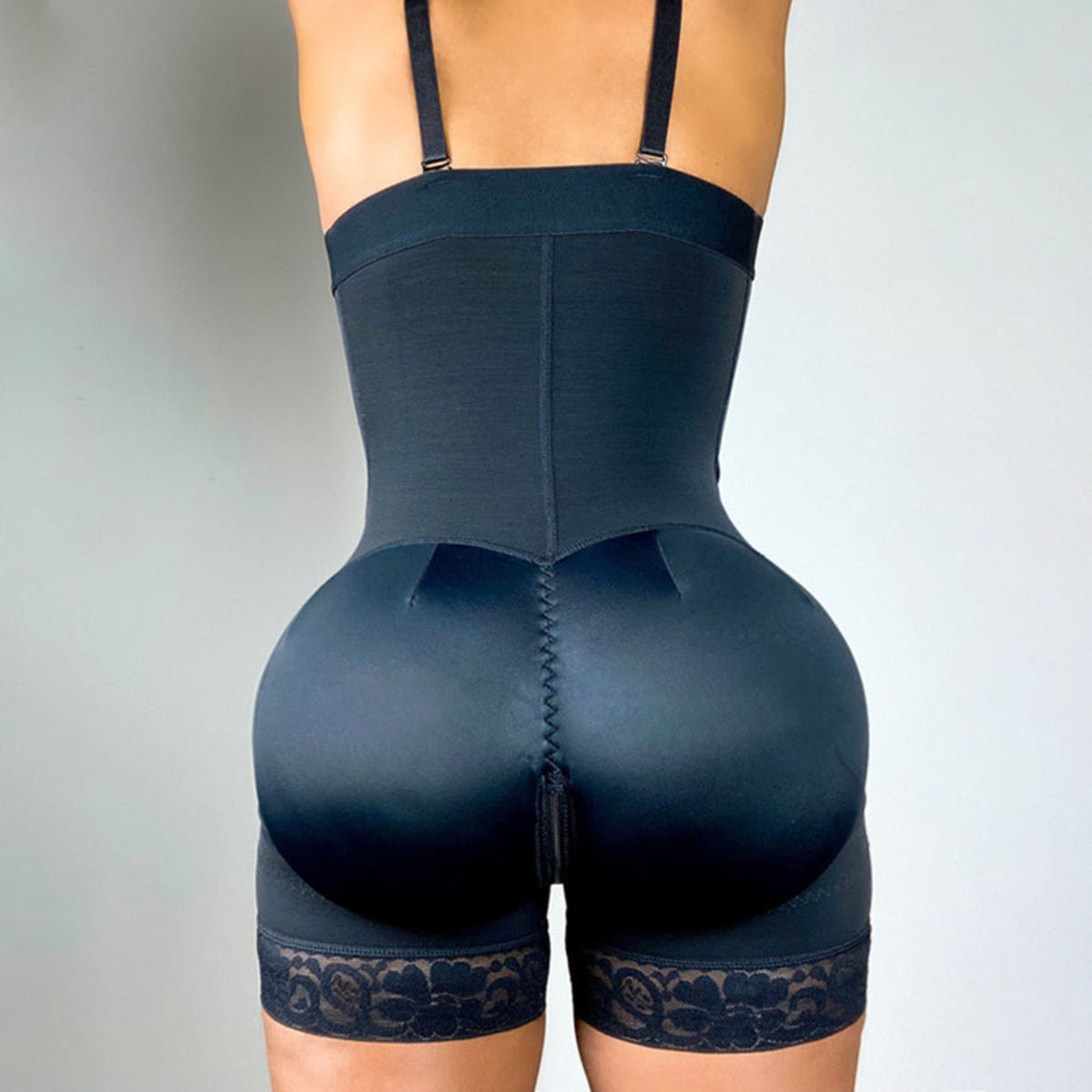 Women's black full-body shapewear with waist control, butt-lifting design, adjustable straps and lace thigh trim shown from the back