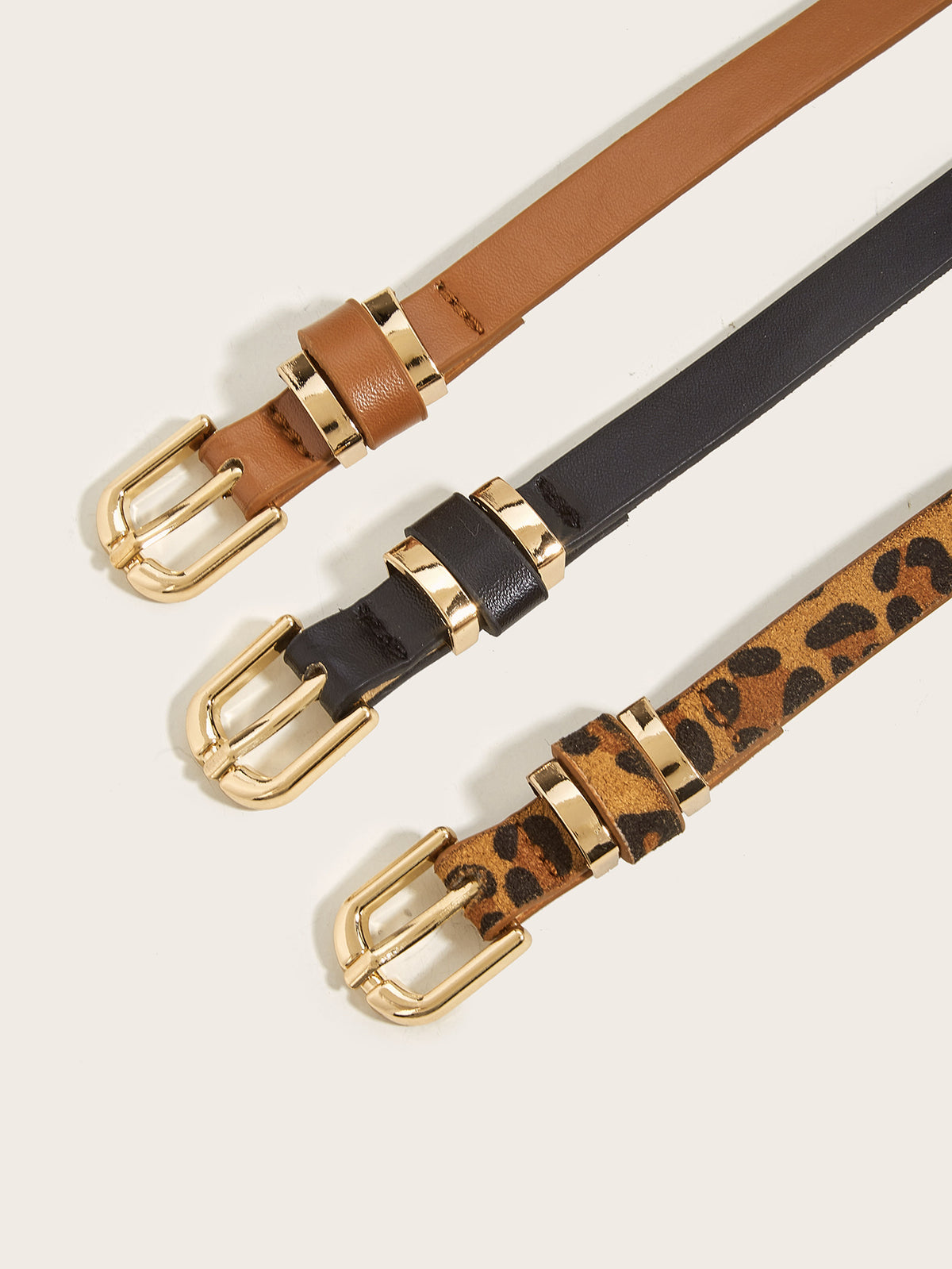 Close-up of women’s skinny belts in black, cognac brown, and leopard print with polished gold-tone buckles