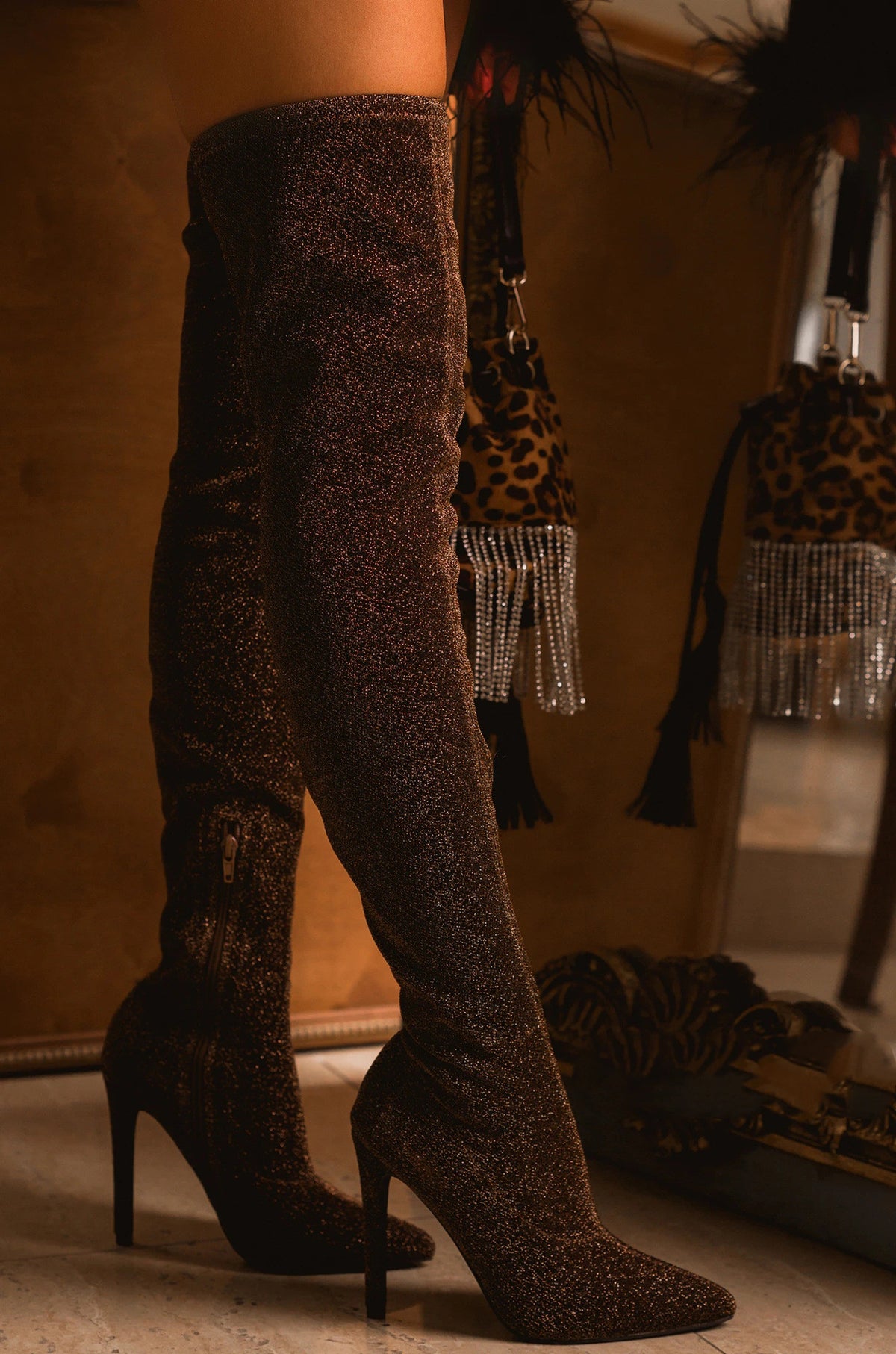 Zaria Bronze Shimmer Over-the-Knee Stiletto Boots worn on a model, featuring a rich deep bronze-brown metallic shimmer finish, fitted thigh-high silhouette, sleek pointed toes, side zipper detail, and elegant slim stiletto heels for a glamorous Fall and Winter statement look.